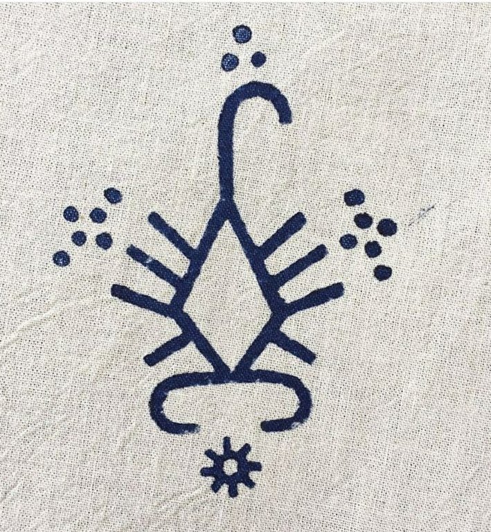 A hand-drawn Warli glyph in indigo on woven linen.