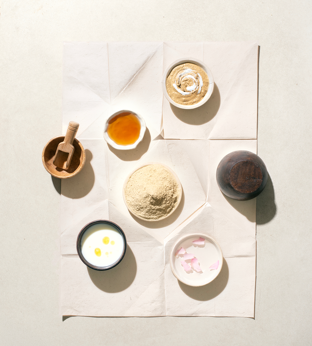 Bowls of honey, milk, rose water and ubtan powder laid on folded paper.