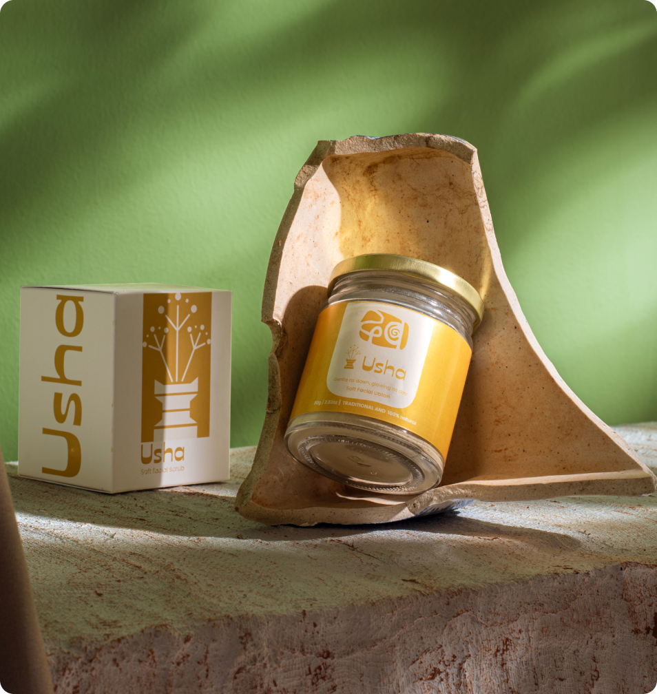 A jar of Usha with its box, resting on stone against a green wall.