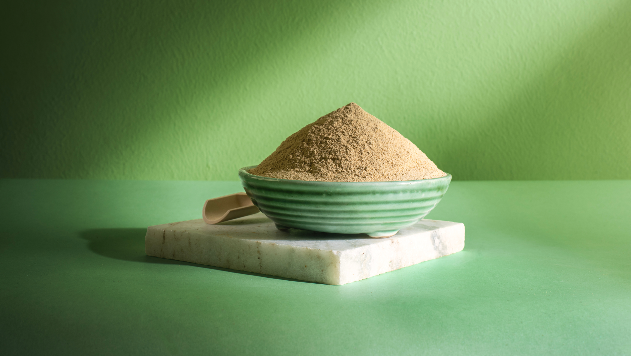 A bowl of Usha ubtan powder on a marble slab against a sunlit green wall.