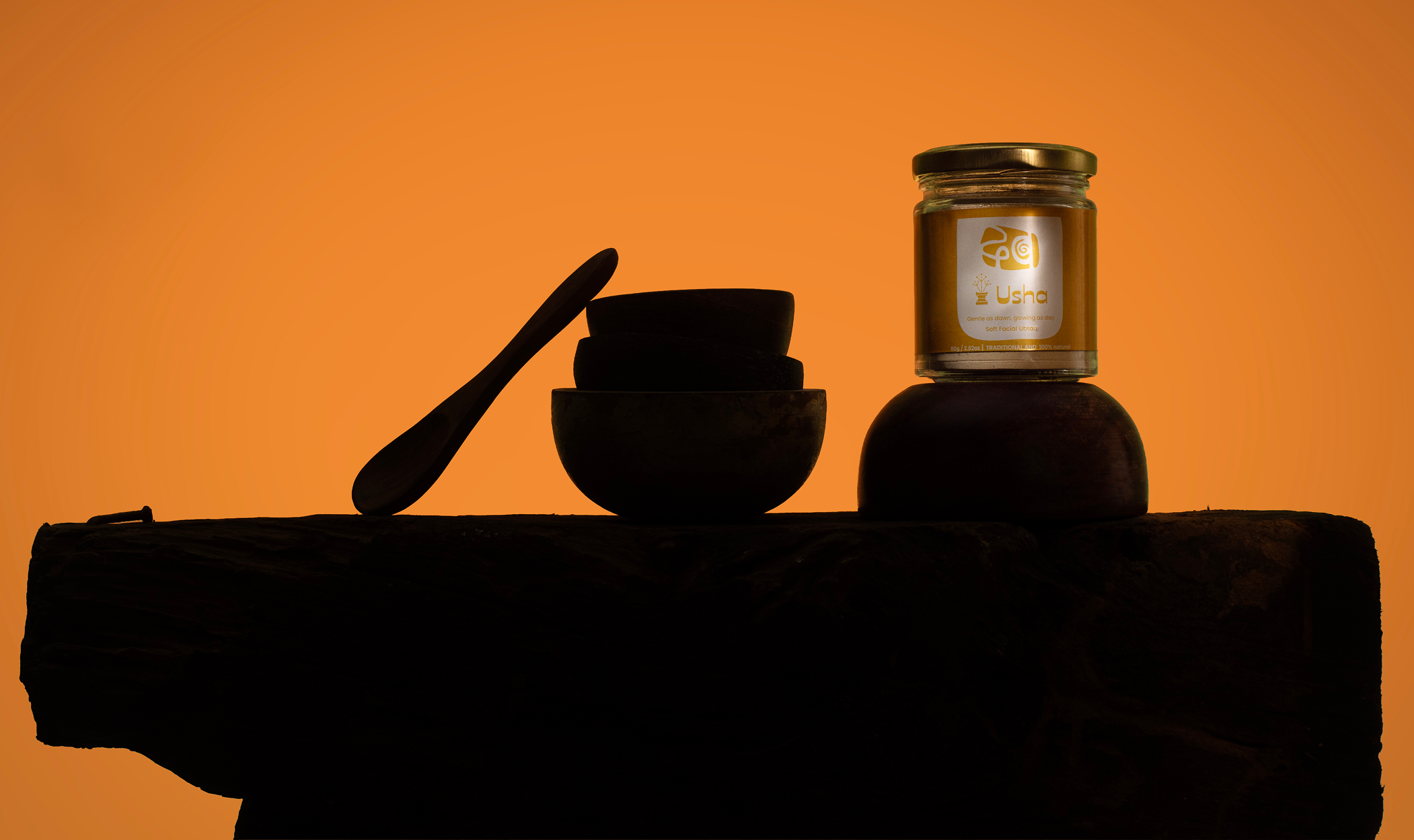 The Usha jar silhouetted with wooden bowls and a spoon against an orange ground.