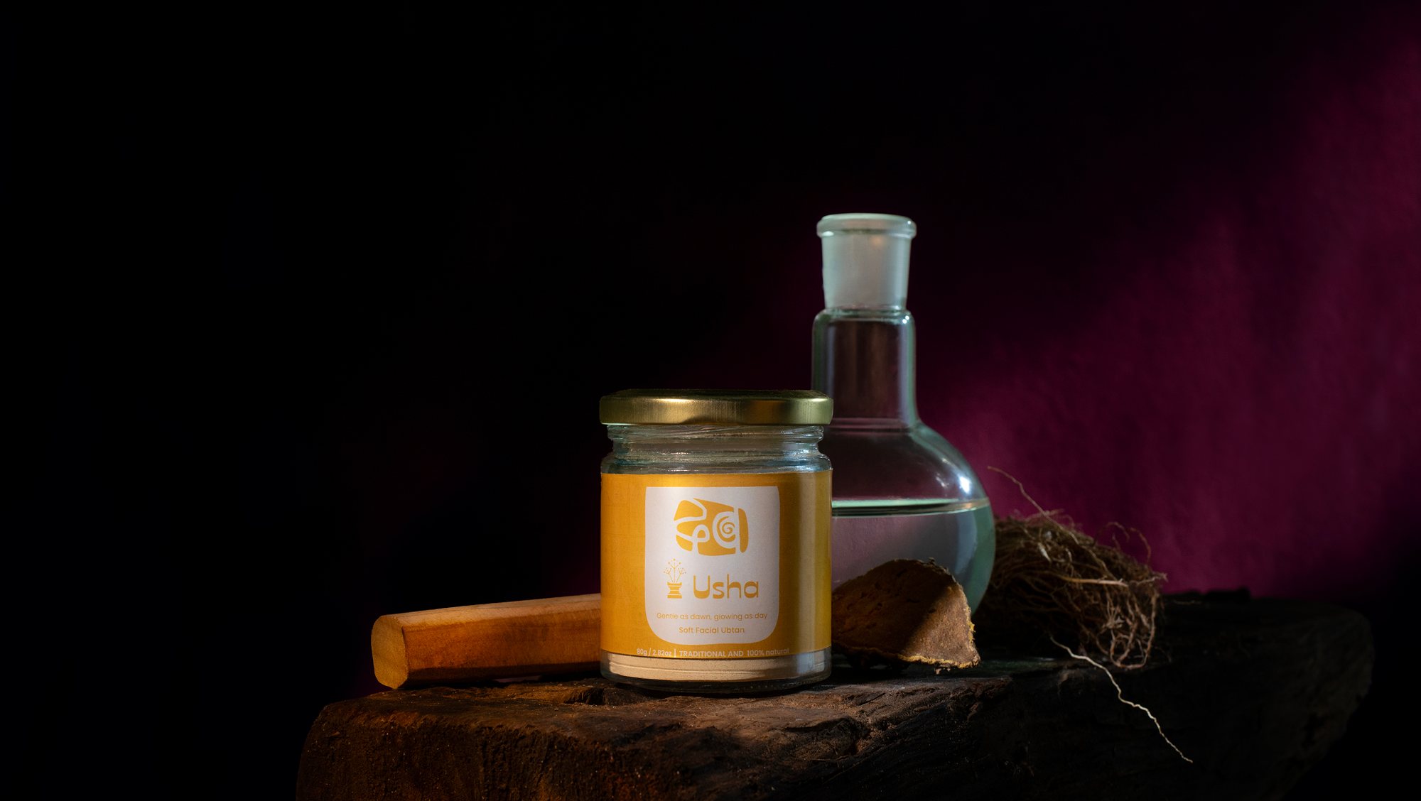A jar of Usha soft facial ubtan beside a glass flask, sandalwood and vetiver root.