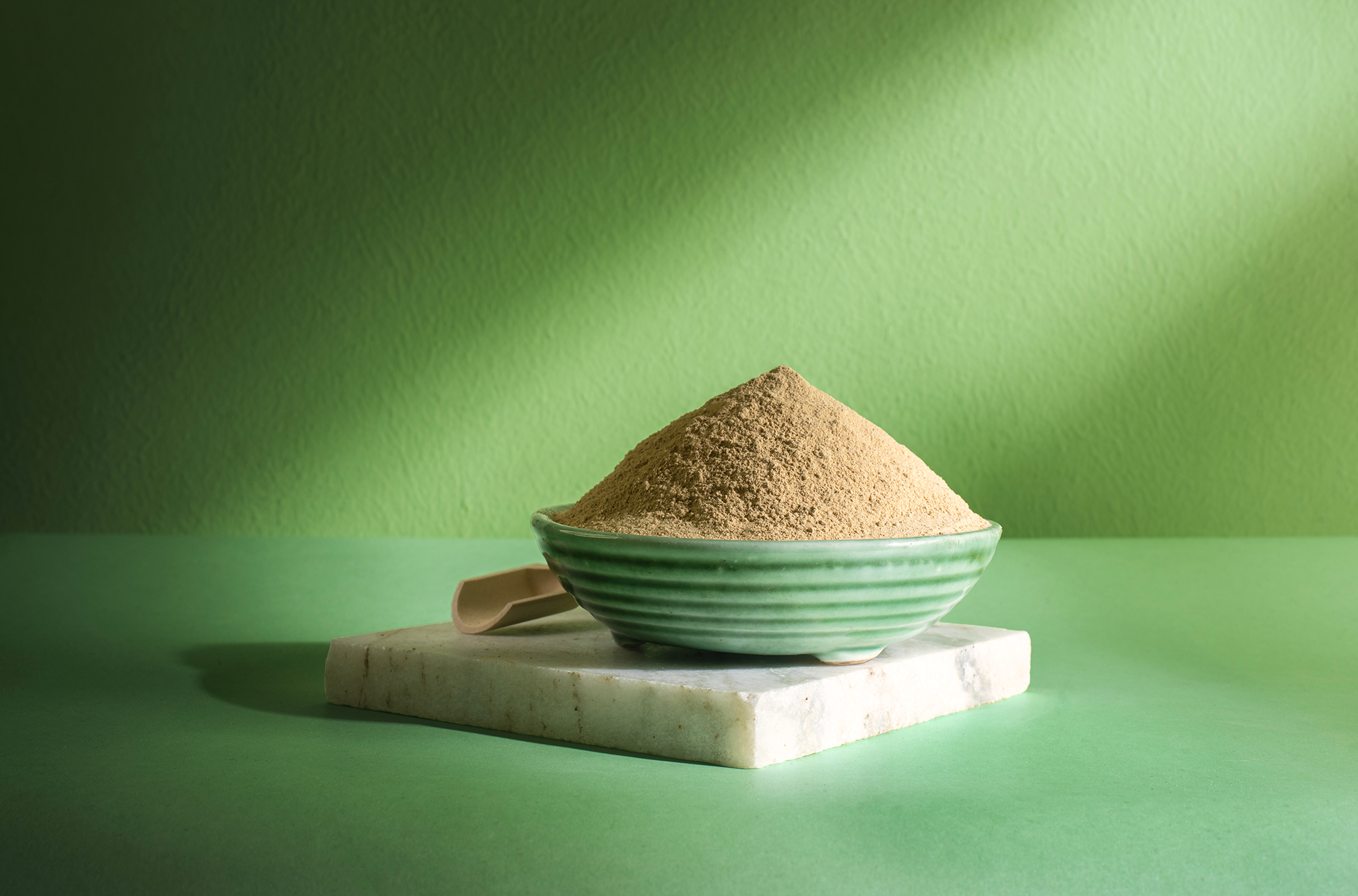 A bowl of ubtan powder on a marble slab against a sunlit green wall.
