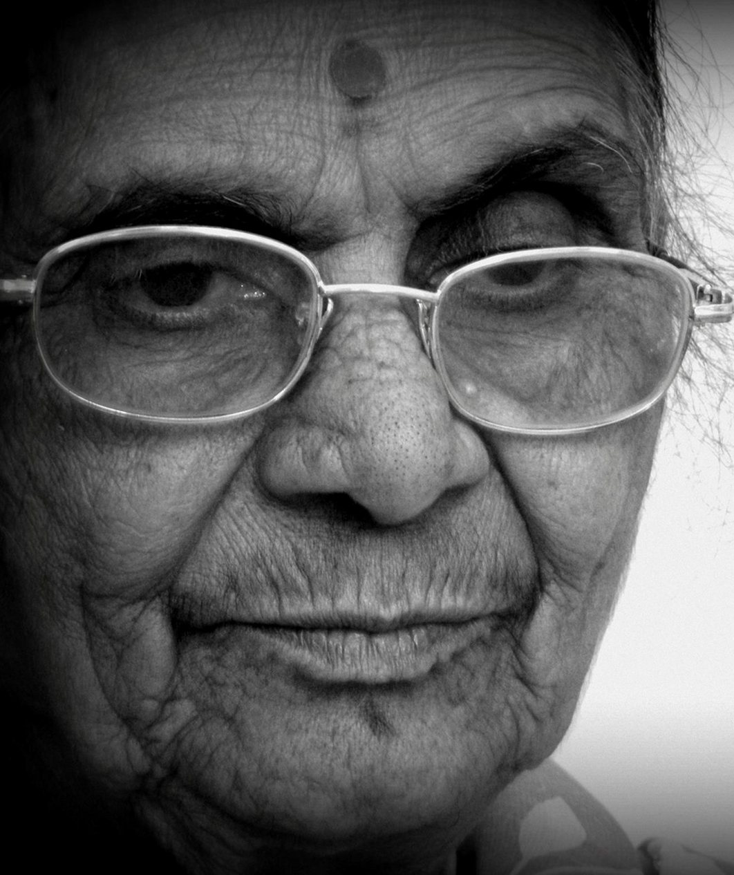 A portrait of an elderly Indian woman in glasses, in black and white.